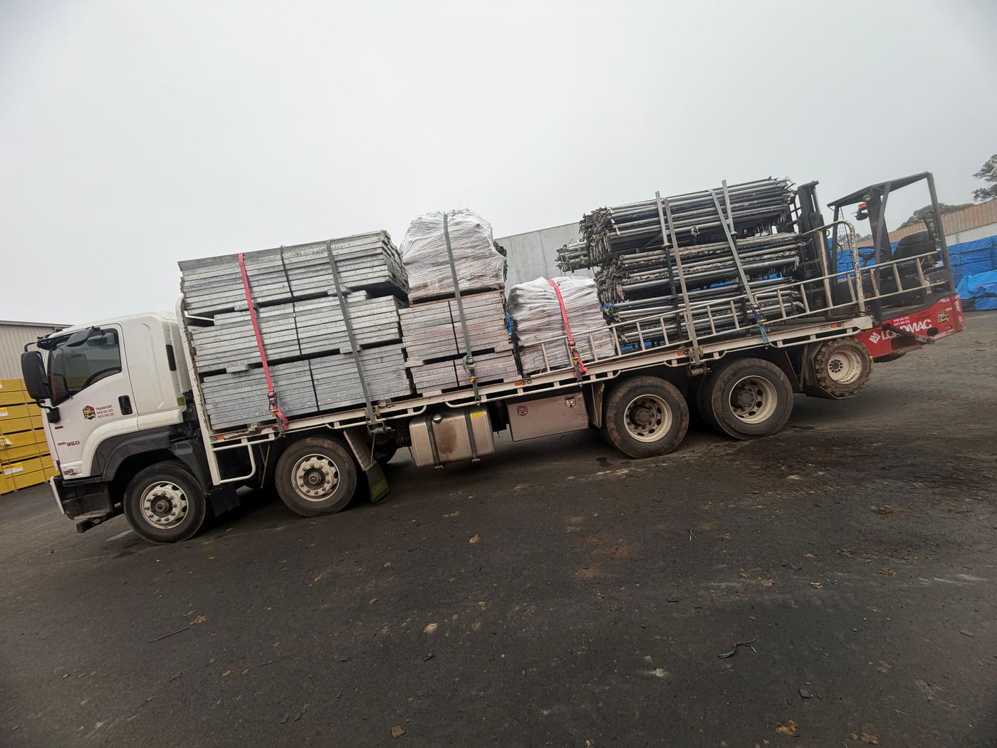 Liberty Transport flatbed truck fully loaded with scaffolding components and buddy forklift mounted on rear